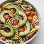 avocado pasta salad in white bowl with tomatoes and herbs