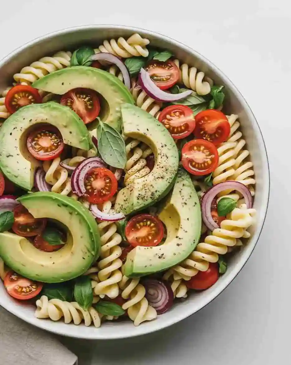 avocado pasta salad in white bowl with tomatoes and herbs